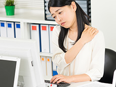 肩こりに悩むパソコン作業中の女性のイメージ